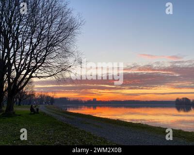 Fiume po e vibrante tramonto sullo sfondo. Il cielo è dipinto in sfumature di arancione, che riflettono l'acqua increspata. San Nazzaro, PC, Italia Foto Stock