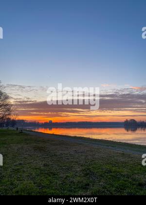 Fiume po e vibrante tramonto sullo sfondo. Il cielo è dipinto in sfumature di arancione, che riflettono l'acqua increspata. San Nazzaro, PC, Italia Foto Stock