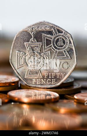 Foto in studio di un pezzo da cinquanta pence in valuta Sterling che mostra la croce victoria in piedi sul tavolo con monete fuori fuoco in primo piano Foto Stock