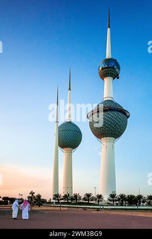 Le torri del Kuwait a Kuwait City e due sceicchi alle spalle discutono e camminano al tramonto Foto Stock