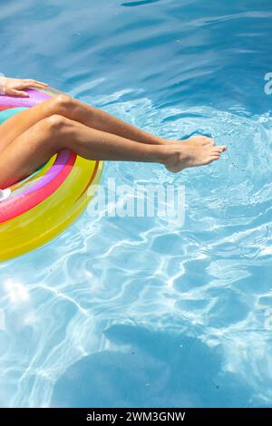 In una giornata di sole, la persona gode di un bagno rilassante in piscina, mentre le gambe riposano su un galleggiante colorato Foto Stock