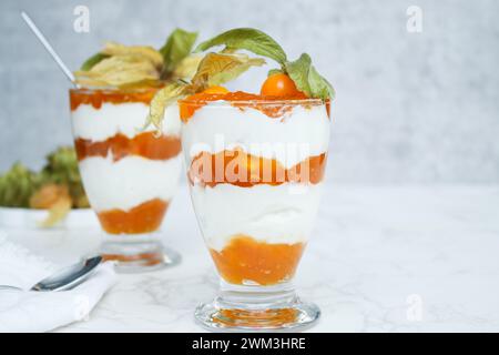 Due bicchieri di dessert stratificato con yogurt proteico e frutta fisalis Foto Stock