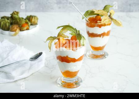 Due bicchieri di dessert stratificato con yogurt proteico e frutta fisalis Foto Stock