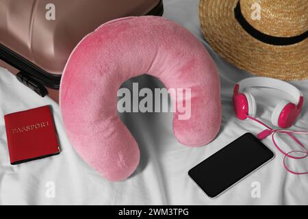 Cuscino da viaggio rosa, valigia, smartphone con cuffie e passaporto sul letto Foto Stock