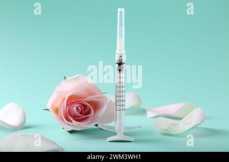 Cosmetologia. Siringa medica, fiore di rosa e petali su sfondo turchese Foto Stock