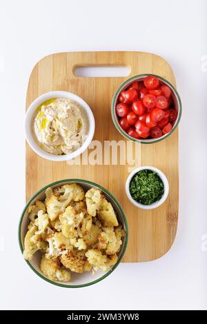 Pomodori di cavolfiore arrostiti e insalata di hummus su sfondo bianco tagliato a legna Foto Stock