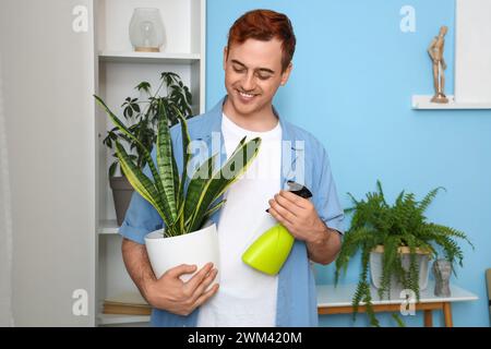 Redhead giovane uomo felice che innaffia piante d'appartamento a casa Foto Stock