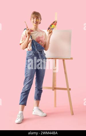 Artista femminile con tavolozza di colori e cavalletto su sfondo rosa Foto Stock