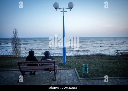 Odessa, Ucraina. 23 febbraio 2024. I passanti siedono di fronte al filo spinato su una passeggiata sulla spiaggia a est di Odessa sul Mar Nero. Vaste parti della costa Ucraina sono state estratte per proteggersi da un approdo russo. Il 24 febbraio 2024 segna il secondo anniversario dell'inizio della guerra di aggressione della Russia contro l'Ucraina. Crediti: Kay Nietfeld/dpa/Alamy Live News Foto Stock