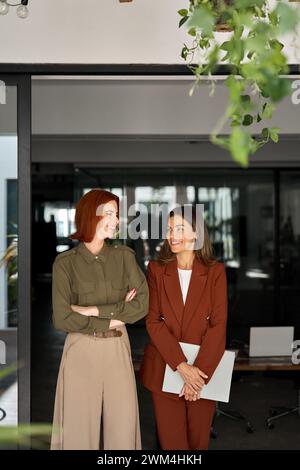 Due donne d'affari felici in piedi al lavoro in ufficio che si guardano l'un l'altra. Foto Stock
