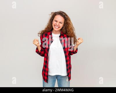 Giovane donna adulta con capelli marroni che indossa una camicia casual rossa si rallegra di fronte a una parete di colore grigio chiaro. Foto Stock