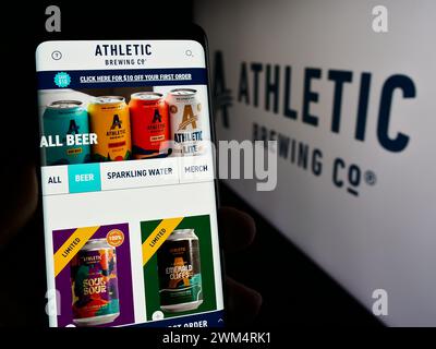 Persona che tiene lo smartphone con la pagina Web della società statunitense di bevande Athletic Brewing Company davanti al logo. Messa a fuoco al centro del display del telefono. Foto Stock