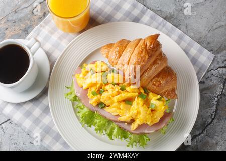 Colazione Croissant Sandwich con uova strapazzate e prosciutto servito con succo d'arancia e caffè da vicino su un tavolo di marmo. Vista dall'alto orizzontale da abov Foto Stock