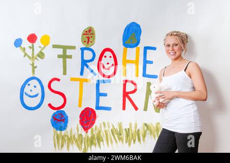 Junge attrattivo Frau vor einer Osterbotschaft Frohe Ostern auf eine Wand gepinselt *** giovane donna attraente di fronte ad un messaggio di Pasqua buona Pasqua dipinta su un muro Foto Stock