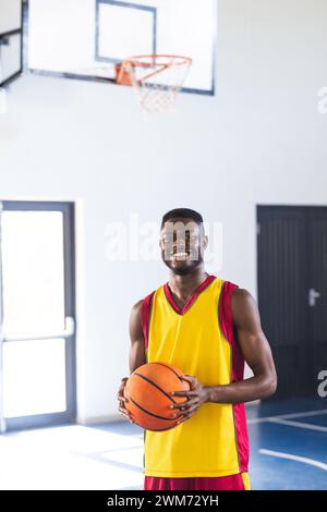 Un giovane afroamericano tiene una pallacanestro in una palestra, con spazio fotocopie Foto Stock