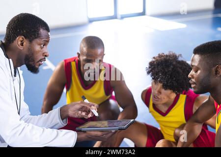 Allenatore afroamericano che discute strategia con i giocatori di basket sul campo Foto Stock