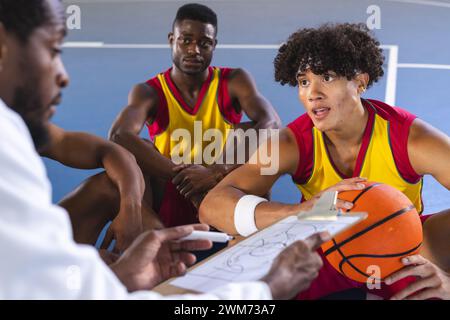 Allenatore di pallacanestro che discute la strategia con i giocatori sul campo Foto Stock