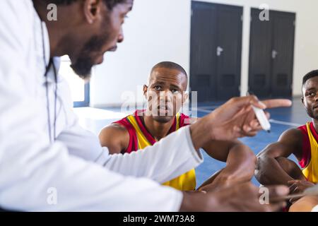 Allenatore afroamericano che discute strategia con i giocatori in una palestra Foto Stock