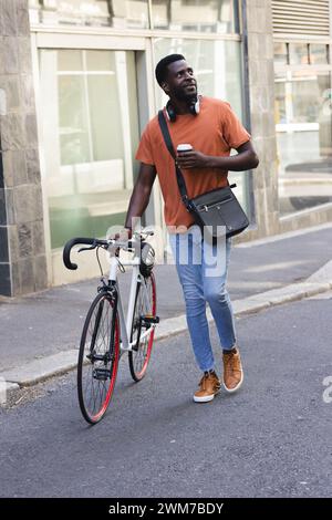 Il giovane afroamericano sta in piedi con la sua bicicletta in una strada cittadina Foto Stock