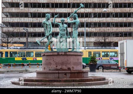 Statua dei tre fabbri, progettata da Felix Nylund, con edificio per uffici Aktian talo in demolizione sullo sfondo a Helsinki, Finlandia Foto Stock