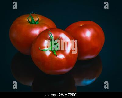 Tre pomodori rossi maturi con riflessi su sfondo nero Foto Stock