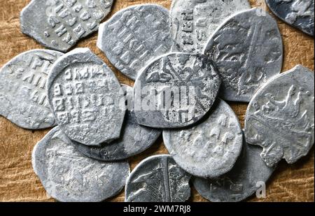 Antiche monete russe primo piano del XVI secolo, mucchio di monete d'argento dello zar Ivan IV il terribile. Vista dall'alto dei fiocchi di metallo su sfondo vintage. Concep Foto Stock