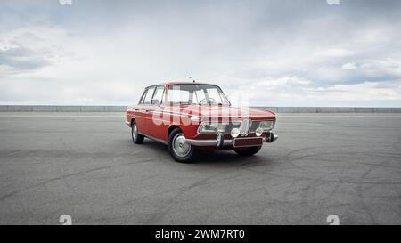BMW rossa classica degli anni '1960 Vista di tre quarti della berlina tedesca di fronte al cielo nuvoloso. Foto Stock