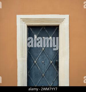 Esterno di una vecchia casa marrone con porta di ferro dipinta di blu indaco. Sportello blu con barre in metallo forgiato in stile rombo e cornice bianca. Foto Stock