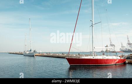 Due yacht nel porto vuoto in una giornata di sole. Calma mattinata di sole al porto marittimo durante la bassa stagione. Yacht rosso e bianco ormeggiato al molo. Foto Stock