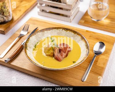 Zuppa di patate in stile moderno con patate al forno e prosciutto affumicato su un elegante tavolo del ristorante Foto Stock