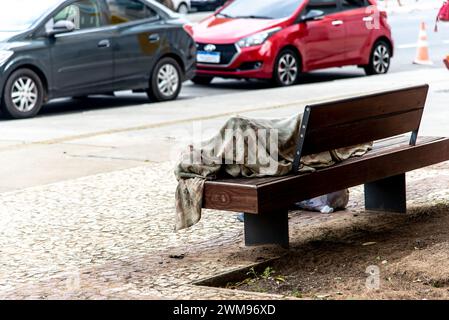Salvador, Bahia, Brasile - 5 gennaio 2024: Un senzatetto dorme su una panchina di legno nel quartiere Comercio nella città di Salvador, Ba Foto Stock