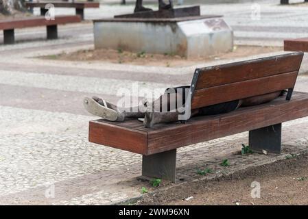 Salvador, Bahia, Brasile - 5 gennaio 2024: Un senzatetto dorme su una panchina di legno nel quartiere Comercio nella città di Salvador, Bahia. Foto Stock