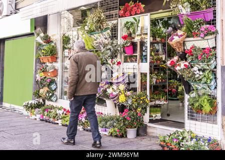 Un uomo che passeggia lungo una strada di fronte alla facciata di un negozio di fiori locale pieno di piante fresche Foto Stock