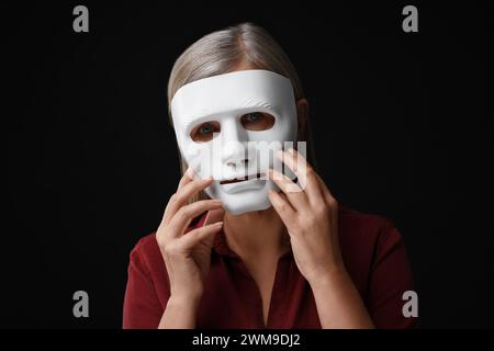 Concetto di personalità multipla. Donna in maschera su sfondo nero Foto Stock