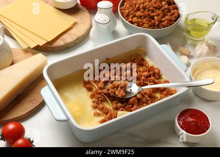 Cottura delle lasagne. Fogli di pasta, carne macinata e prodotti in vassoio da forno su tavolo in marmo bianco Foto Stock