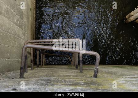 Una scala metallica irregolare con barre incorporate nel calcestruzzo di una struttura quadrata che conduce a un ben riempito d'acqua Foto Stock