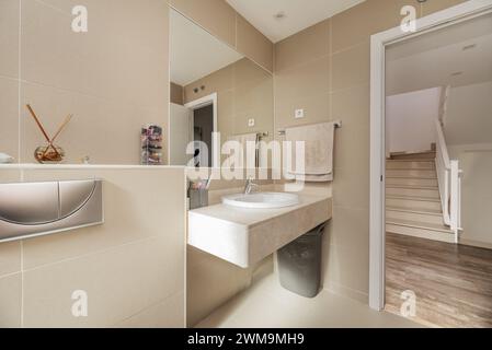 Bagno convenzionale con ripiano in marmo, specchio a parete, piastrelle color crema e porte bianche Foto Stock