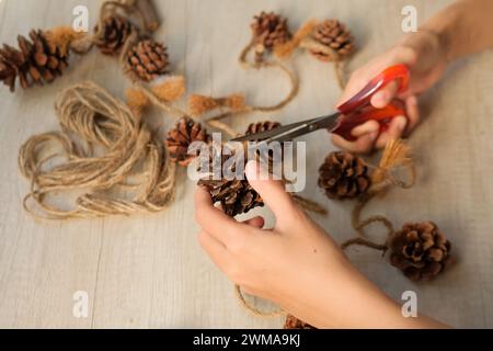 Le mani delle donne creano decorazioni murali con coni di pino e corda di iuta Foto Stock