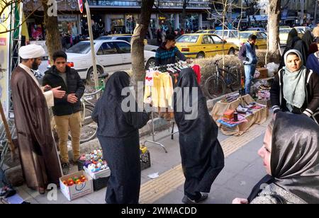 Un mullah parla con un venditore ambulante ad Arak, in Iran, donna che indossa abiti tradizionali e chadors il 16 marzo 2019. Dopo il ritiro degli Stati Uniti dal Foto Stock