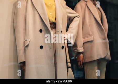 Eleganti manichini in una vetrina vestita con un panno alla moda di stagione. Cappotto beige e camicia giallo brillante. Foto Stock