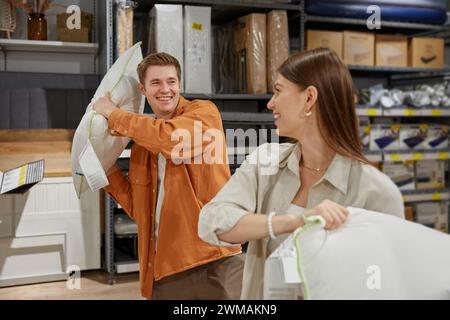 Felice felicemente felice coppia di uomini e donne che combattono cuscino al negozio di biancheria Foto Stock