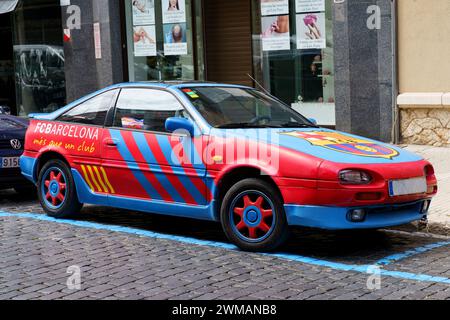 Figueres, Spagna - 14 maggio 2023: Una vivace auto rossa e blu, decorata con il logo del FC Barcelona e i temi di design, è parcheggiata dal marciapiede su un urba Foto Stock