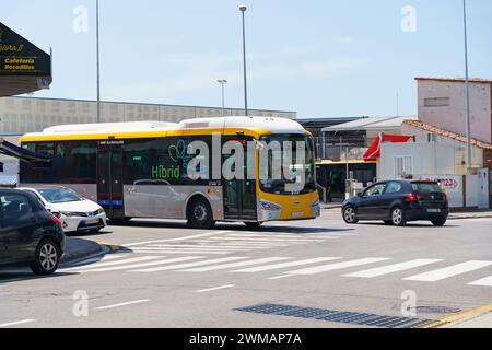 Barcellona, Spagna - 8 maggio 2023: Un autobus ibrido giallo gira all'incrocio, vicino ai magazzini di un'area portuale. I veicoli attendono al semaforo Foto Stock