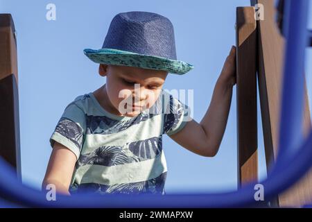 Un bambino sale in un parco giochi in una calda giornata estiva. Parco giochi per bambini in un parco pubblico, animazione e svago per i bambini. Foto Stock