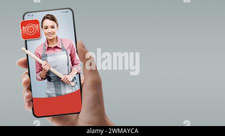 Cuoca donna con una biforcetta sullo smartphone: Noleggia professionisti online Foto Stock