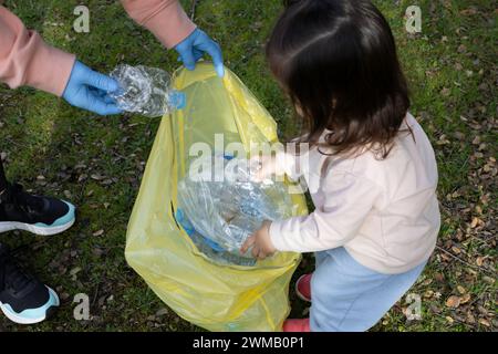 La giovane madre con sua figlia ricicla bottiglie di plastica e le mette in un sacchetto giallo della spazzatura. Concetto di riciclaggio, maternità, volontariato Foto Stock