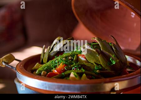 Carciofi e verdure condite con erbe di coriandolo e prezzemolo tritate, servite in tradizionale piatto di argilla tagine marocchina. Informazioni sul blog del cibo Foto Stock