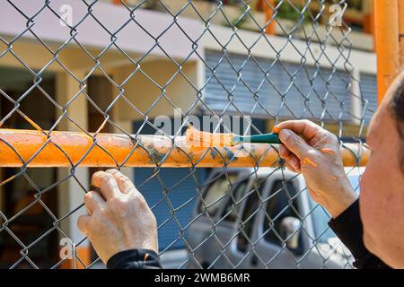 Mano corta di uomo che dipinge il colore su una recinzione a catena Foto Stock