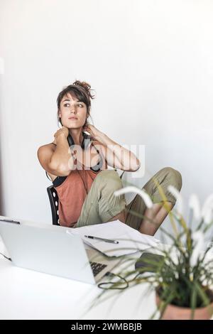 Una giovane donna si prende una pausa dal suo lavoro creativo, i suoi pensieri si spostano mentre gira una penna, le cuffie intorno al collo, un momento di riflessione in mezzo Foto Stock