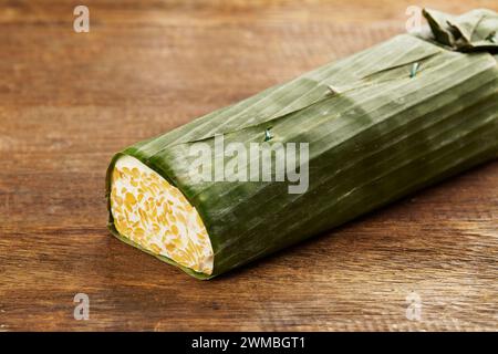 un pezzo di tempeh crudo avvolto in foglie di banana su un tavolo di legno Foto Stock